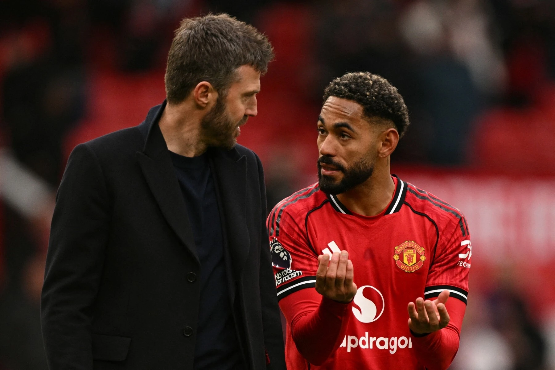 Matheus Cunha trong áo đỏ Man Utd vừa nói vừa giơ hai tay về phía Michael Carrick mặc áo khoác đen