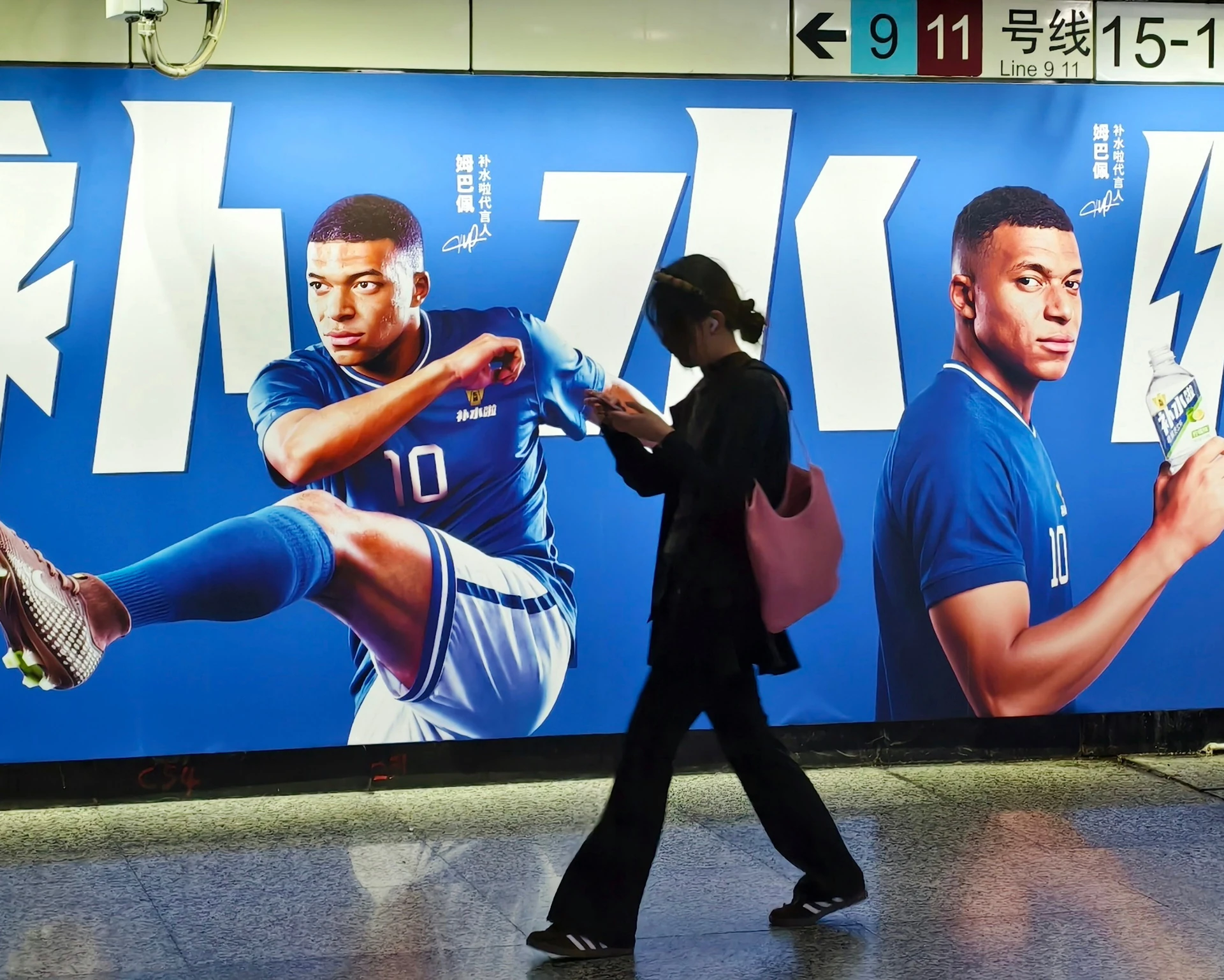 Một người đi bộ qua tấm quảng cáo có hình Kylian Mbappé tại Thượng Hải.