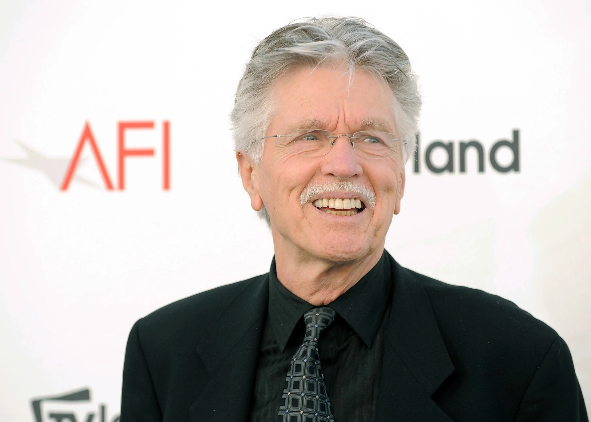Ảnh tư liệu năm 2012: Tom Skerritt tóc bạc, đeo kính, mặc đồ đen, cười trước phông nền có chữ AFI tại một sự kiện ở California.