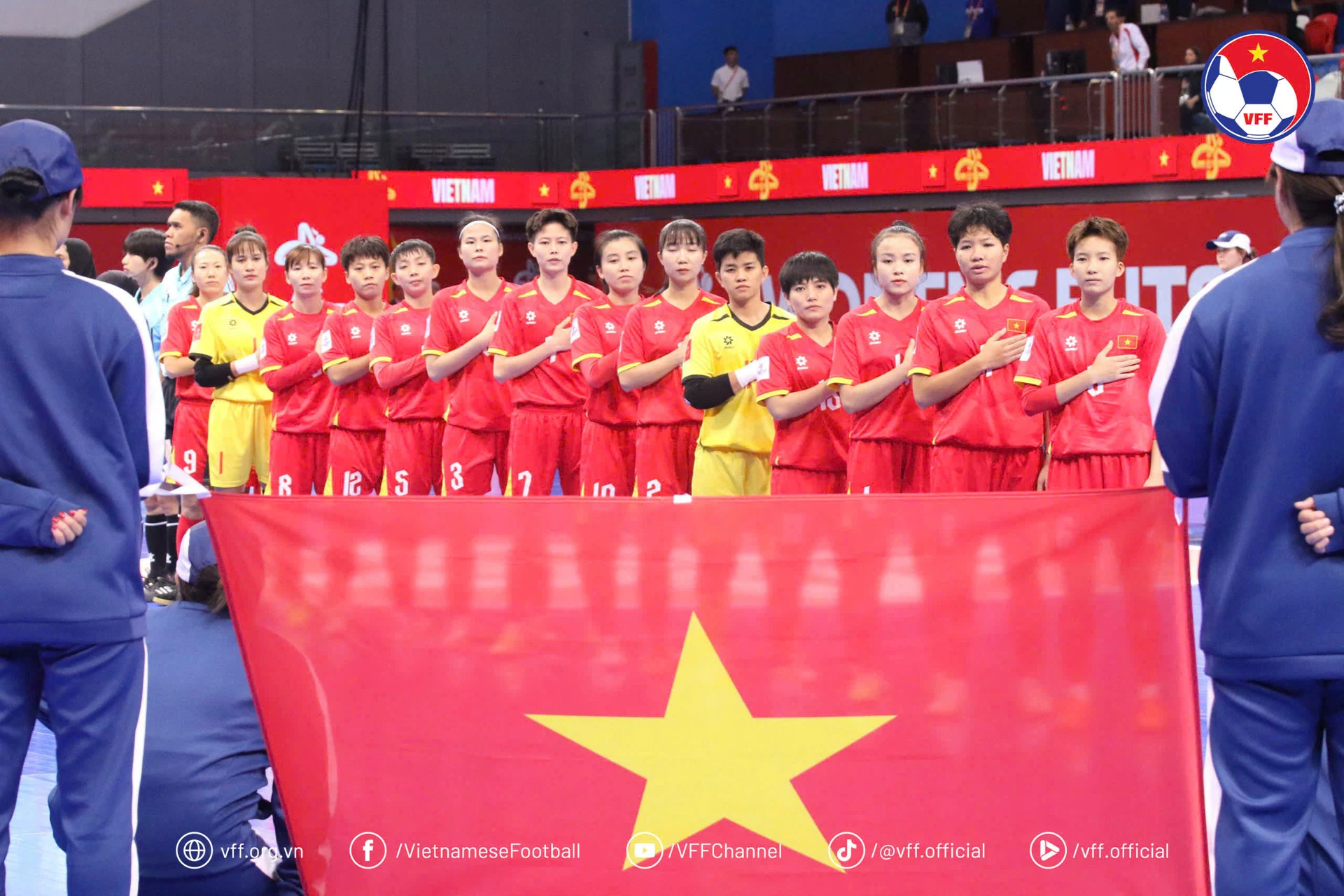 Vietnam women's futsal players stand for the anthem behind a Vietnamese flag.