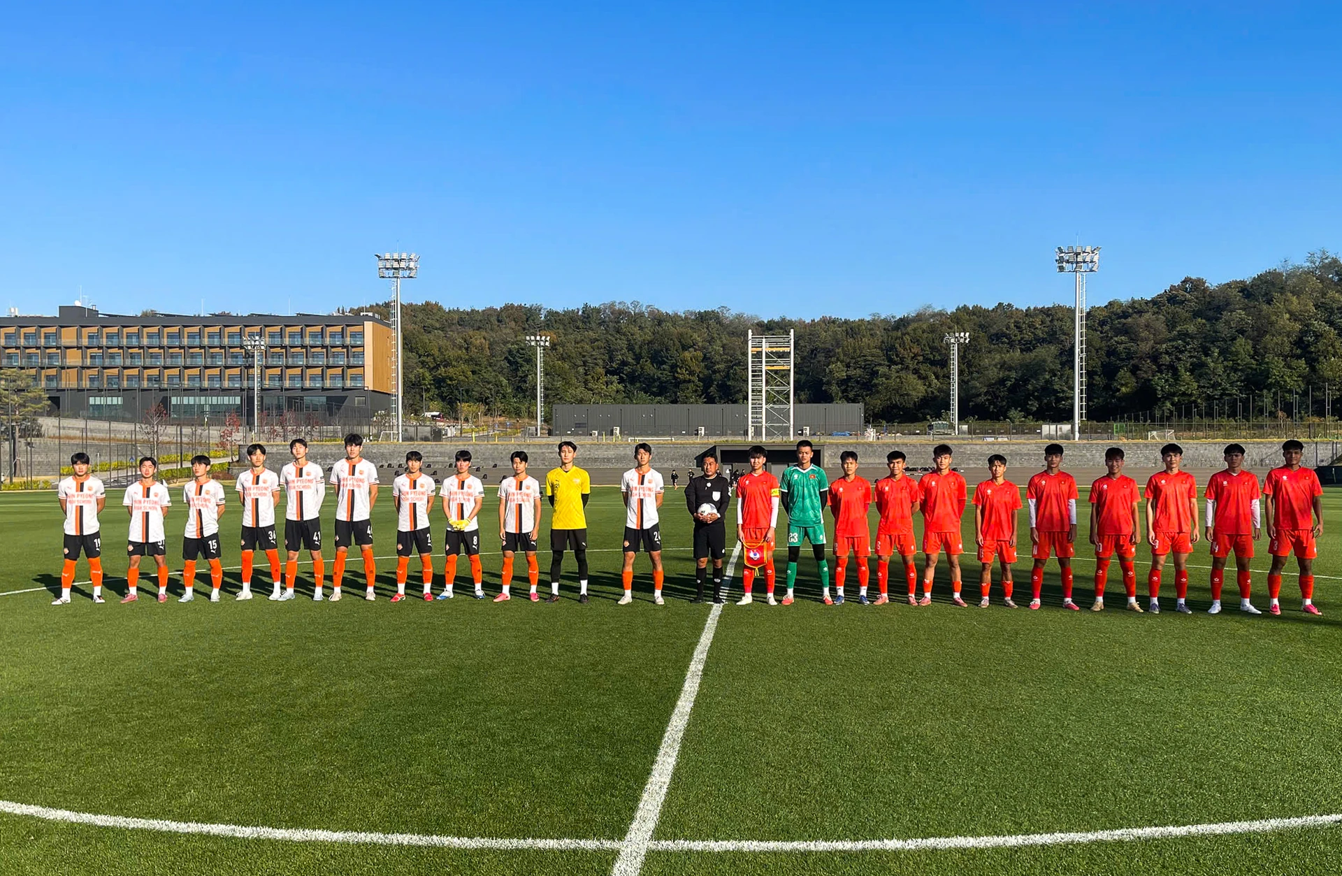U17 Việt Nam (áo đỏ) và CLB Shinpyeong xếp hàng trên sân trước trận đấu tập tại Hàn Quốc.