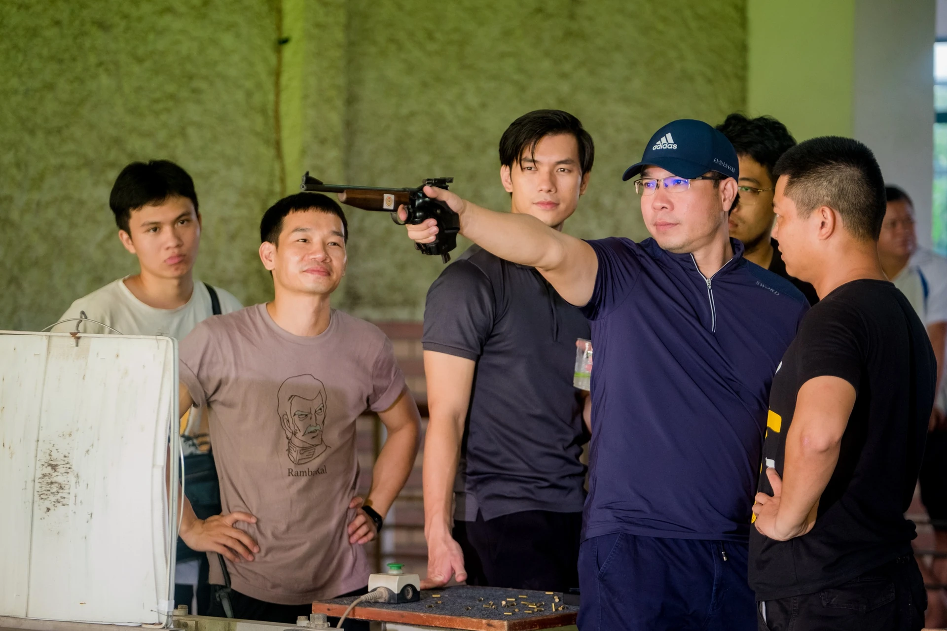 Shooter Hoàng Xuân Vinh demonstrates pistol shooting technique to actor Nhan Phúc Vinh and the film crew.