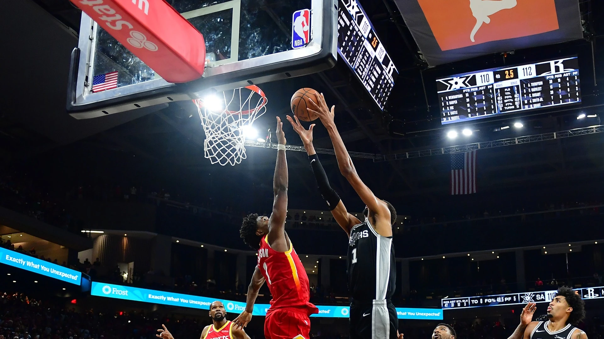 Amen Thompson (áo đỏ số 1 của Rockets) bật cao chắn bóng Victor Wembanyama (áo đen Spurs) dưới rổ trong nhà thi đấu