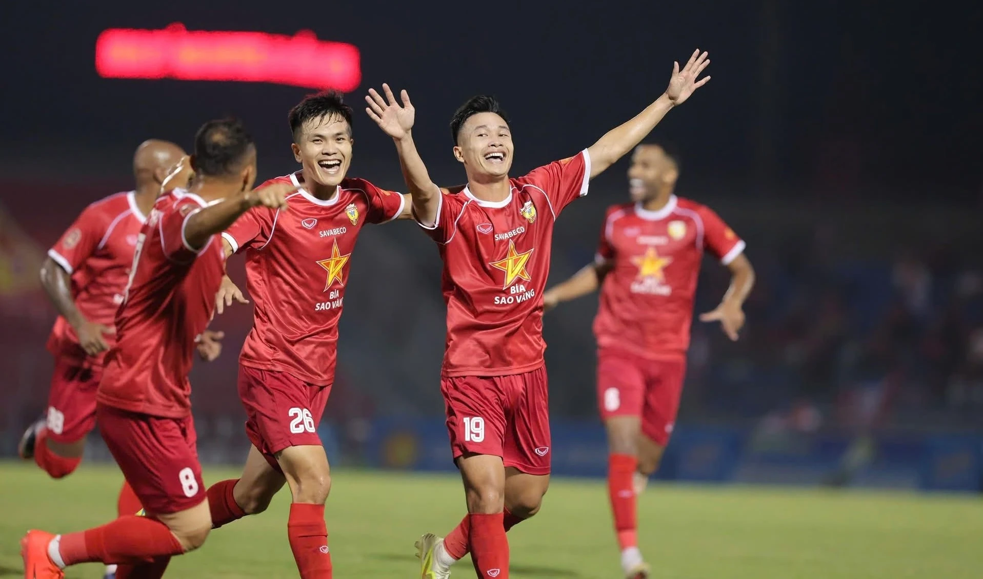 Các cầu thủ Hồng Lĩnh Hà Tĩnh mặc áo đỏ dang tay, cười ăn mừng trên sân vào buổi tối