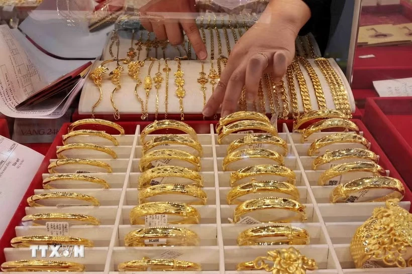 Một nhân viên sắp xếp vòng và lắc tay vàng trang sức trong tủ kính tại một cửa hàng vàng