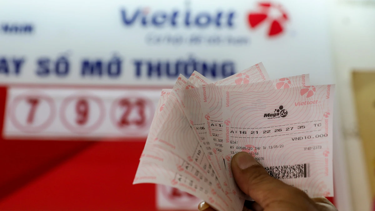 Một người cầm xấp vé xổ số Vietlott trước bảng kết quả quay số mở thưởng