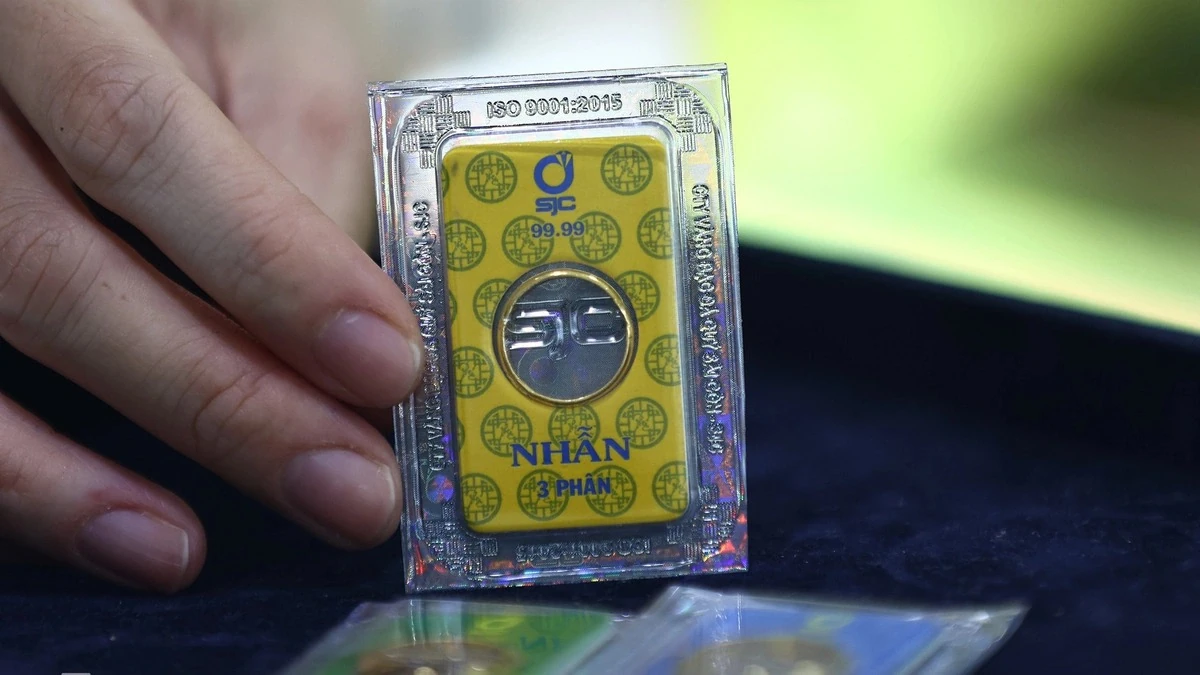 File photo: A hand holds a sealed SJC 99.99 gold piece marked 3 phan, with more gold pieces in the foreground on dark cloth.