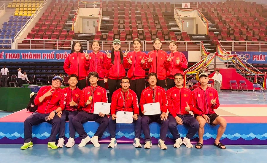 Các thành viên đội tuyển đấu kiếm Việt Nam mặc áo đỏ chụp ảnh tập thể trong nhà thi đấu, một số người cầm giấy chứng nhận và đeo huy chương.