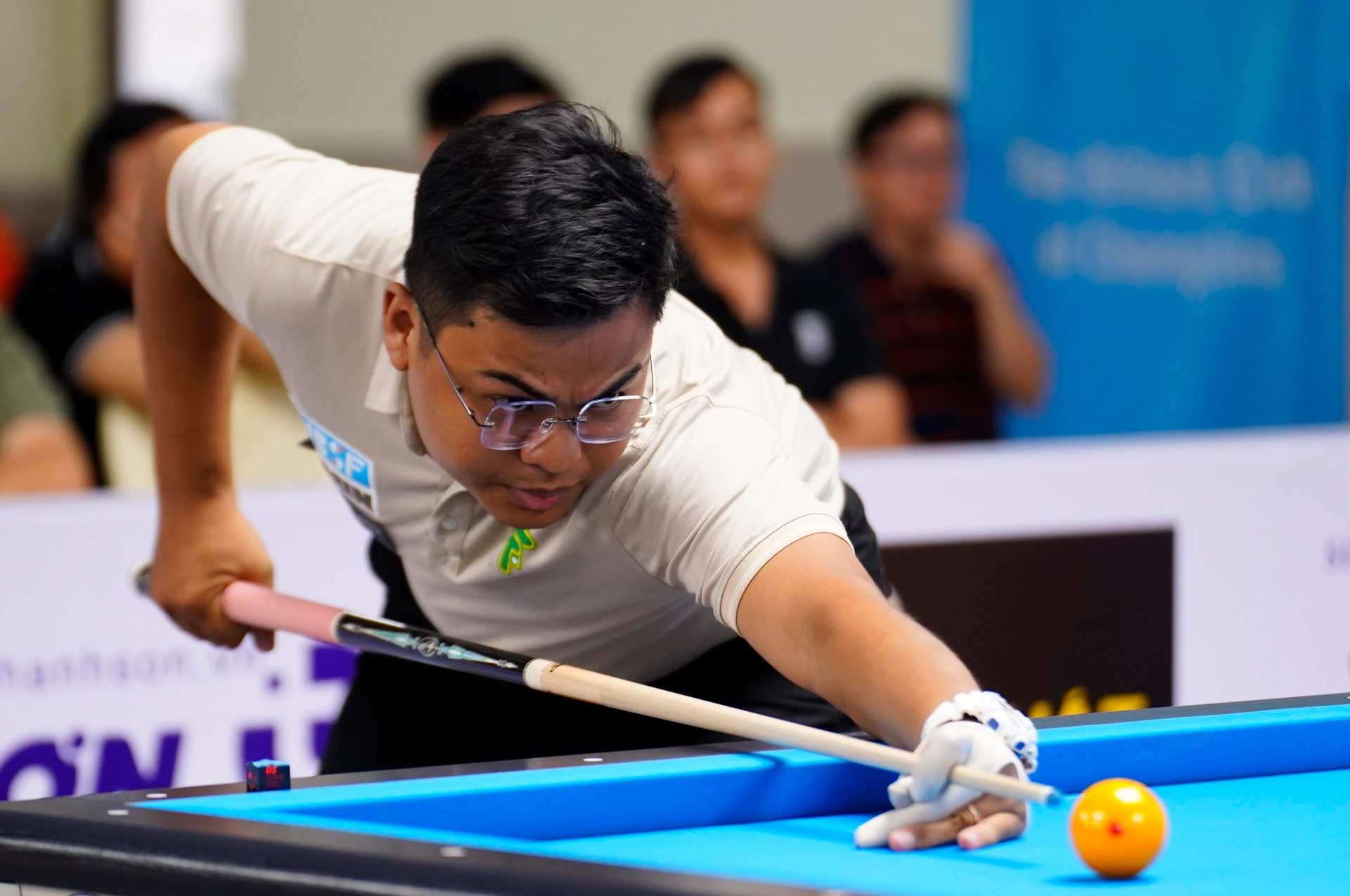 Nguyen Tran Thanh Tao, wearing glasses, leans over the blue billiards table to line up a shot as spectators watch behind him
