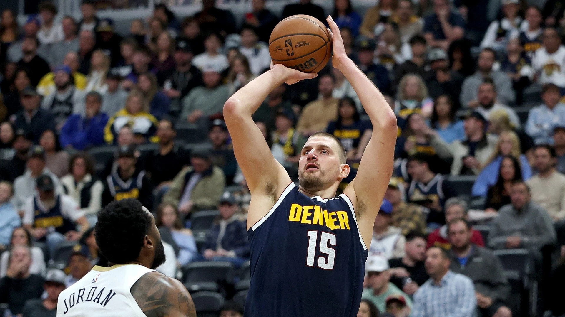 Nikola Jokić (số 15, Denver Nuggets) bật nhảy ném bóng trước một cầu thủ đối phương mặc áo trắng