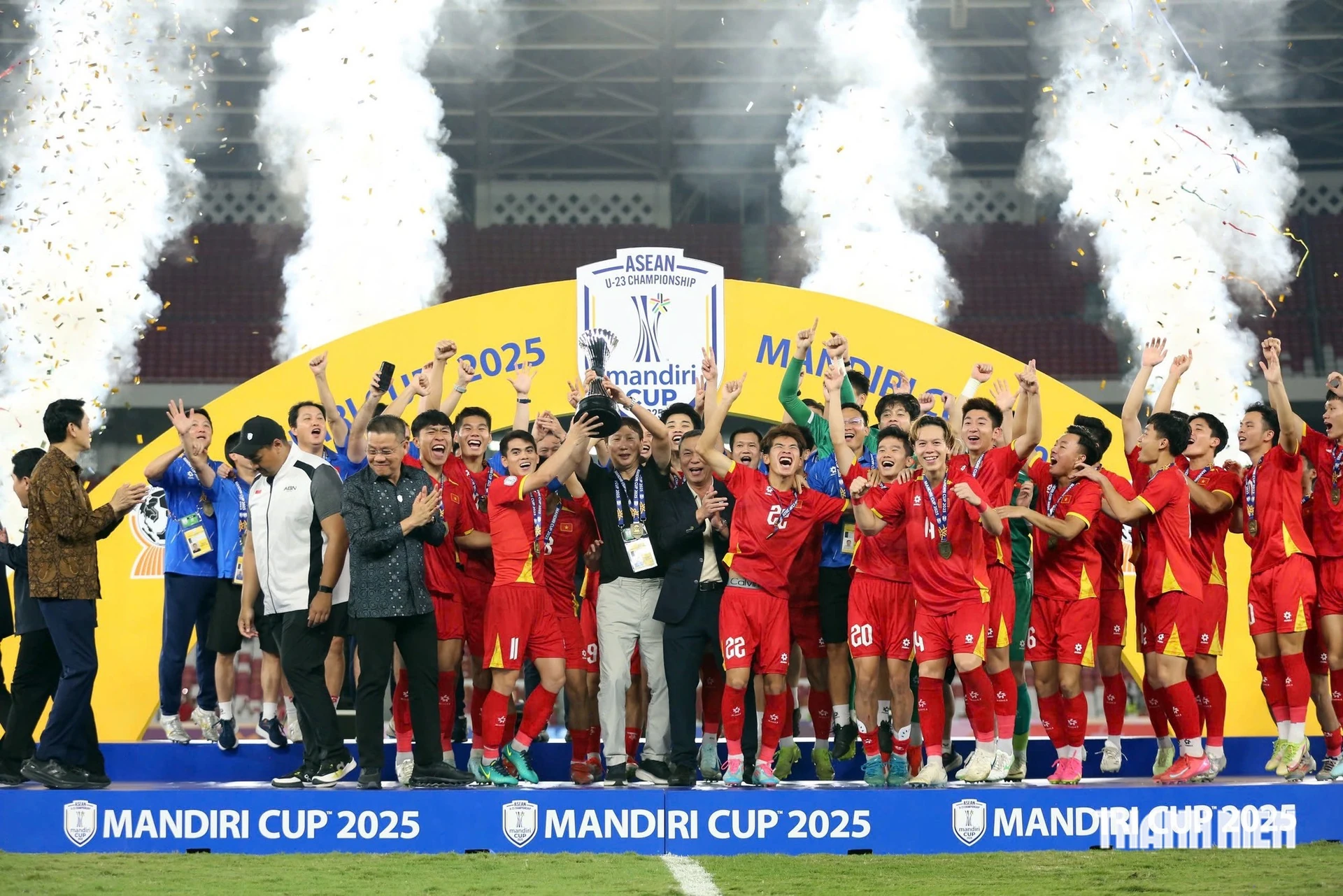 Các cầu thủ U23 Việt Nam áo đỏ nâng cúp vô địch trên bục trao giải Mandiri Cup 2025, pháo hoa và kim tuyến phía sau