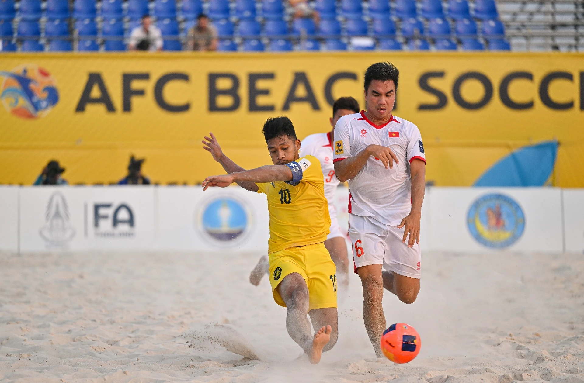 File photo: a Vietnam beach soccer player in white chases the ball while an opponent in yellow slides in on the sand at an AFC tournament match.