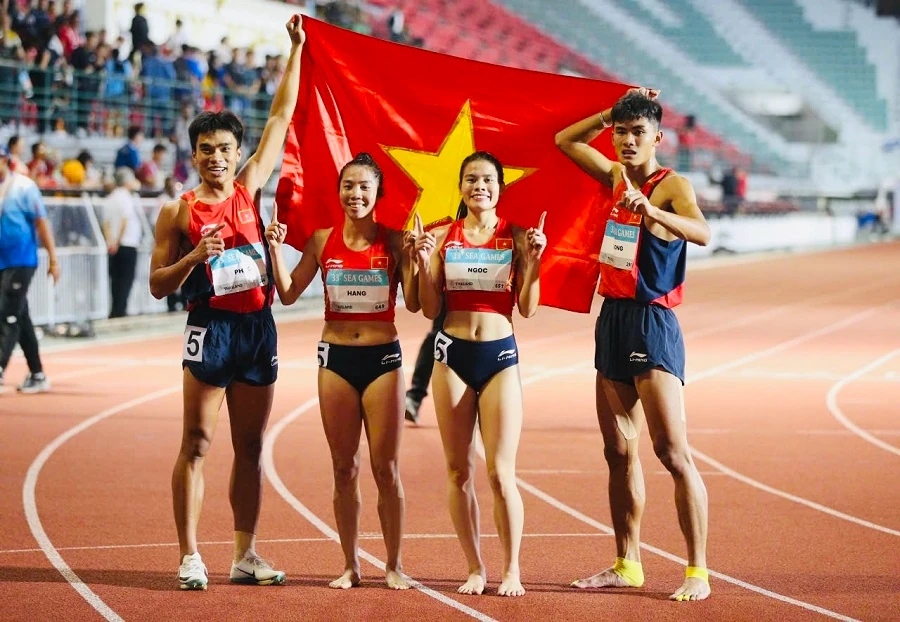 Bốn vận động viên điền kinh Việt Nam căng cờ đỏ sao vàng trên đường chạy sau khi thi đấu